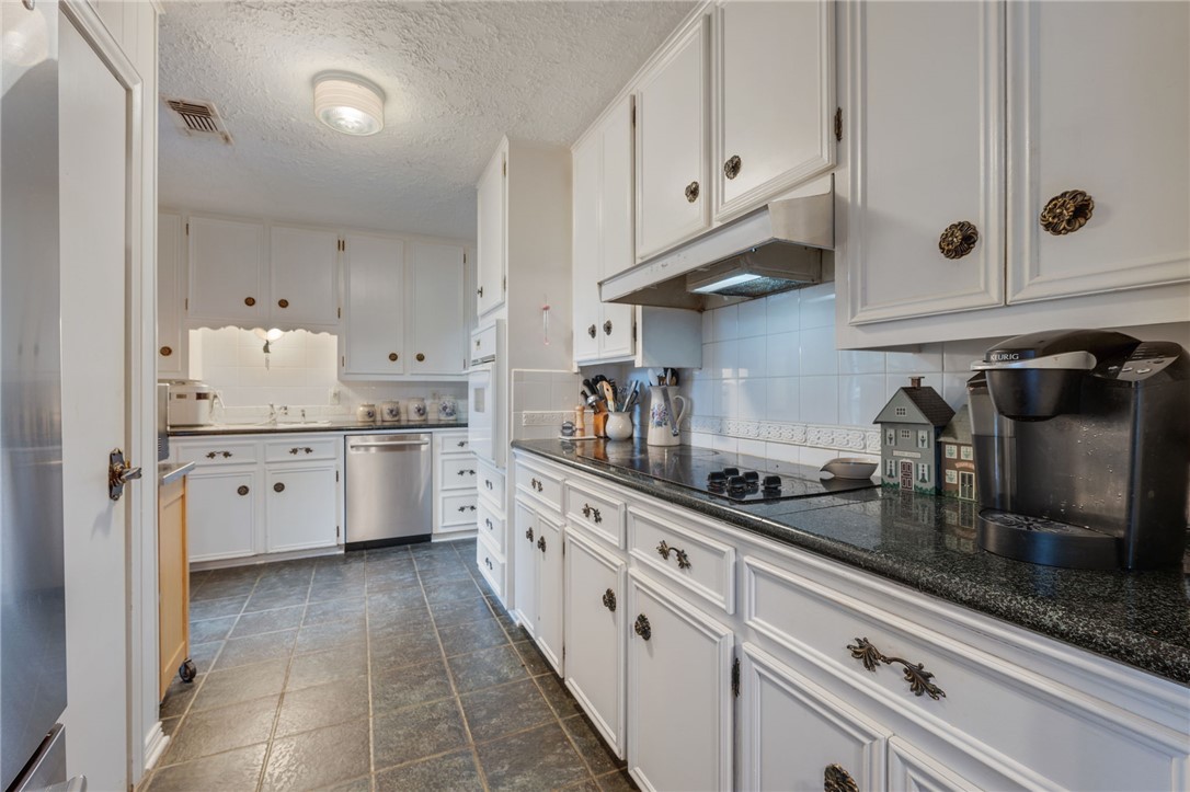 503 Calvert Street Hearne, TX 77859 - Photo 6 of 30 Kitchen featuring backsplash, white cabinetry, under cabinet range hood, stainless steel appliances, and a textured ceiling