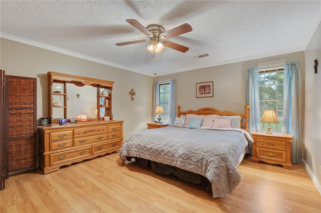 503 Calvert Street Hearne, TX 77859 - Photo 9 of 30 Bedroom with a textured ceiling, light wood-style flooring, ceiling fan, and ornamental molding