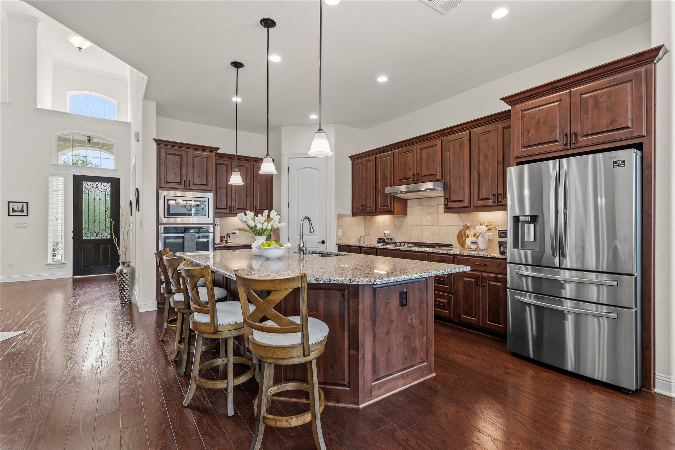1733 Siena Sunset Road Leander, TX 78641 - Photo 16 of 40 Open-concept kitchen featuring dark wood cabinetry, stainless steel appliances, a granite-topped island with seating, and wood-finish flooring