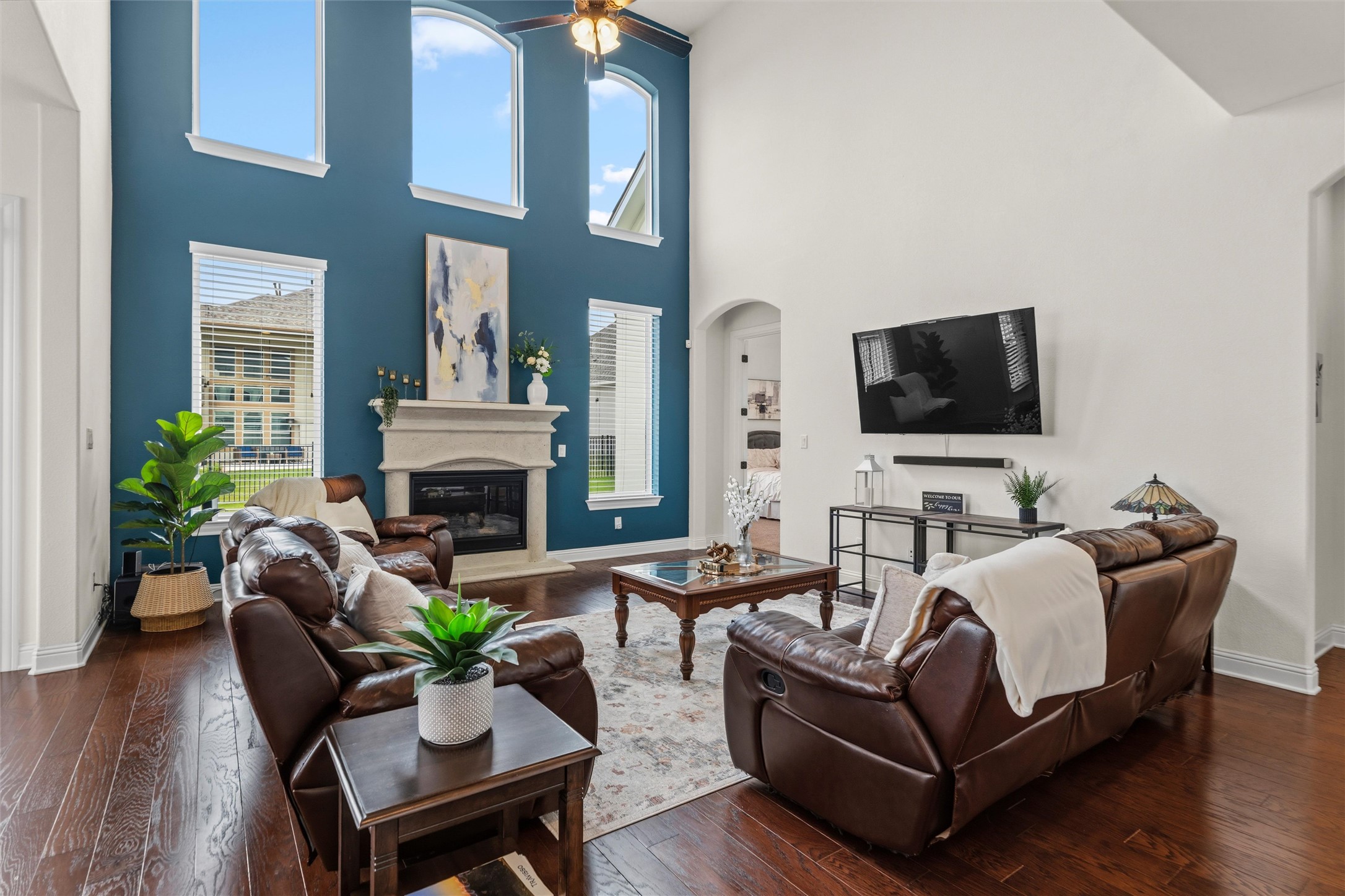 1733 Siena Sunset Road Leander, TX 78641 - Photo 23 of 40 Living space featuring soaring ceilings, a stone-mantled fireplace, abundant natural light from multiple windows, dark wood-finish flooring, and a ceiling fan