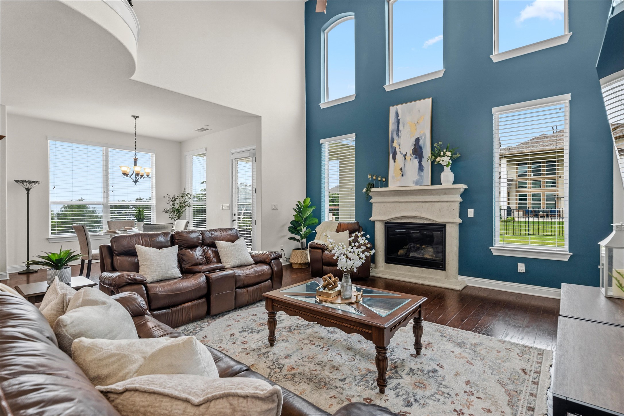 1733 Siena Sunset Road Leander, TX 78641 - Photo 24 of 40 Two-story living area featuring dark wood-finish flooring, a fireplace with a stone mantel, and a multi-story window array