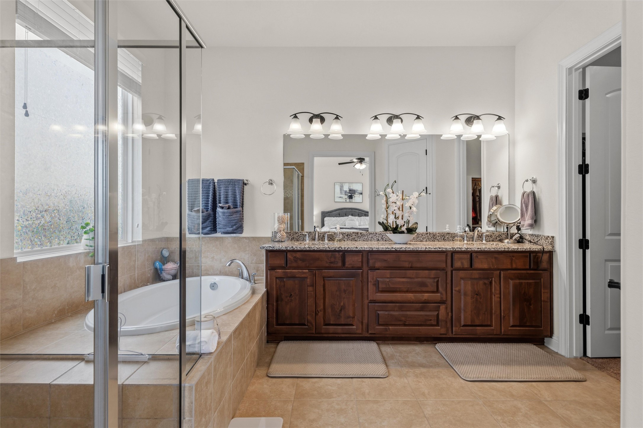 1733 Siena Sunset Road Leander, TX 78641 - Photo 29 of 40 Double vanity with stone countertop and integrated sinks, extensive wood cabinetry, framed mirror with task lighting, tiled flooring, and a separate soaking tub with tiled surround