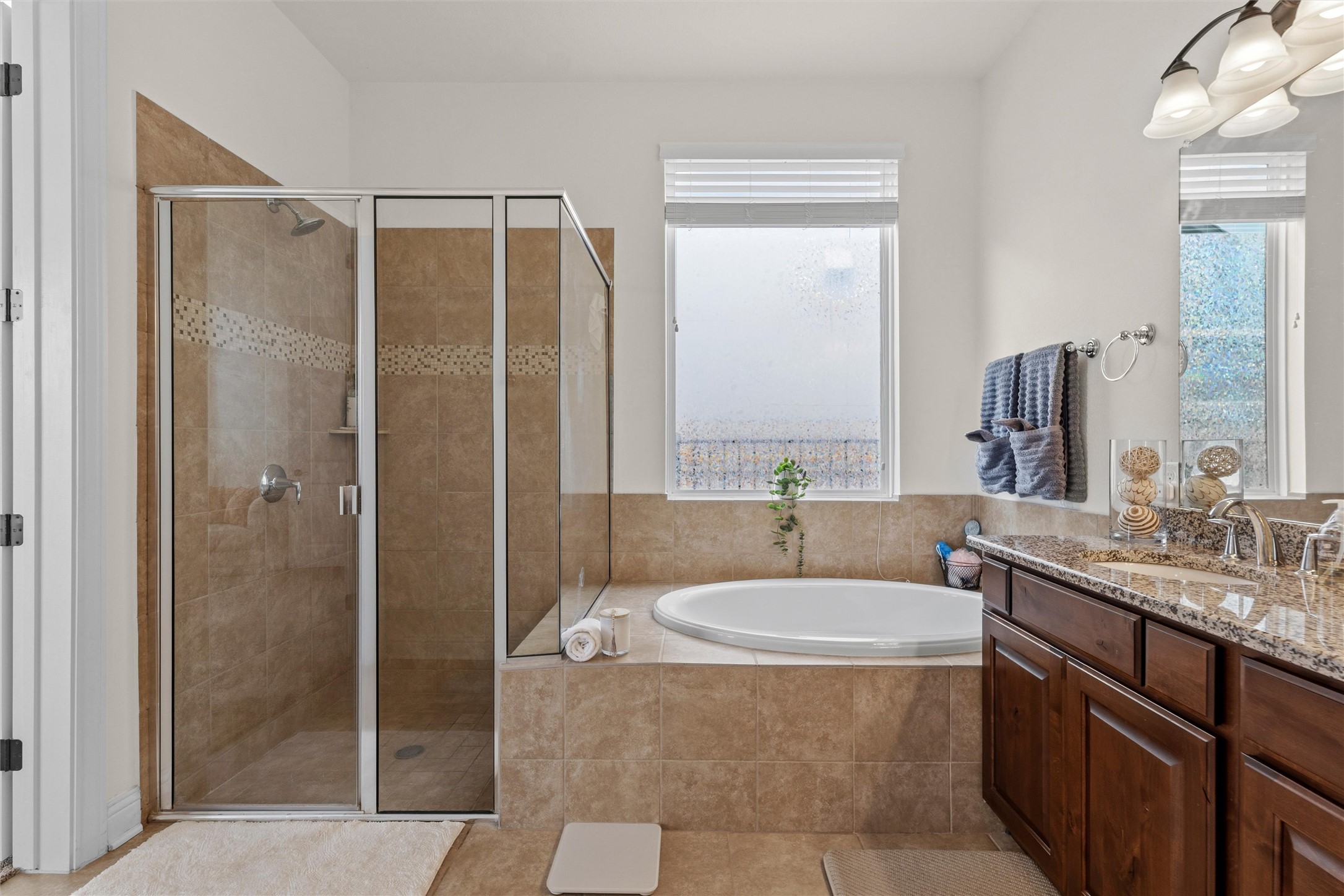 1733 Siena Sunset Road Leander, TX 78641 - Photo 30 of 40 Expansive bathroom featuring a glass-enclosed shower with tiled walls and a decorative accent band, a built-in oval soaking tub, a double vanity with a granite-style countertop, dark wood-finish cabinetry, and a chrome-finish faucet