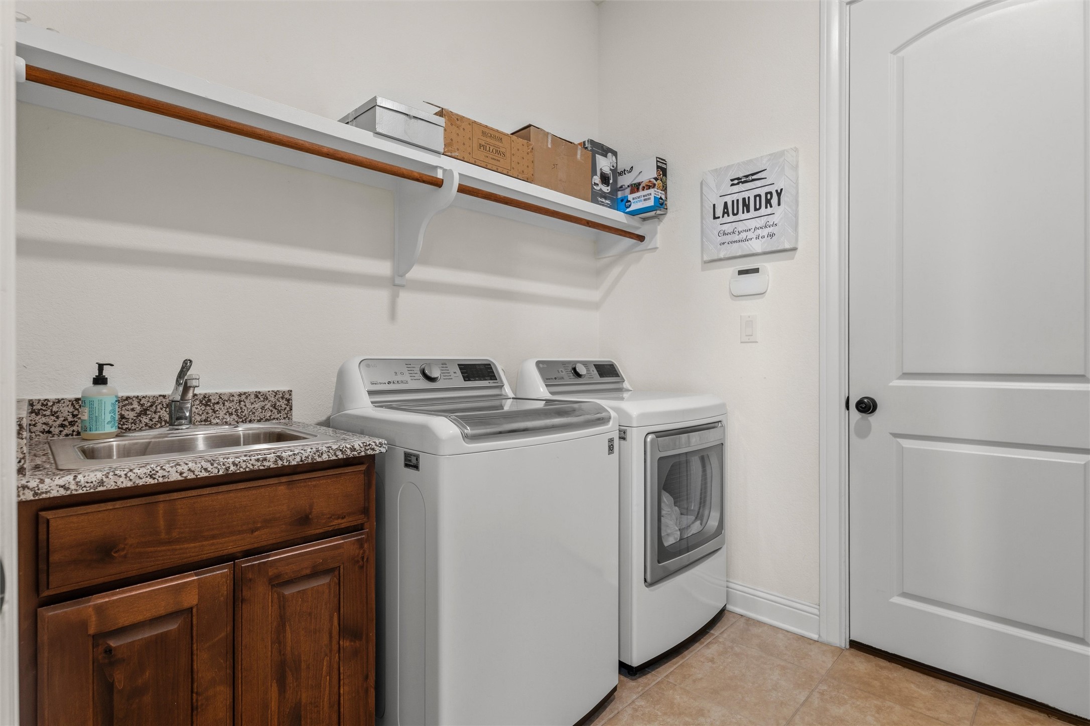 1733 Siena Sunset Road Leander, TX 78641 - Photo 32 of 40 Dedicated laundry space featuring a utility sink with a granite-look countertop, wood-finish cabinetry, upper shelving with a hanging rod, and tile flooring