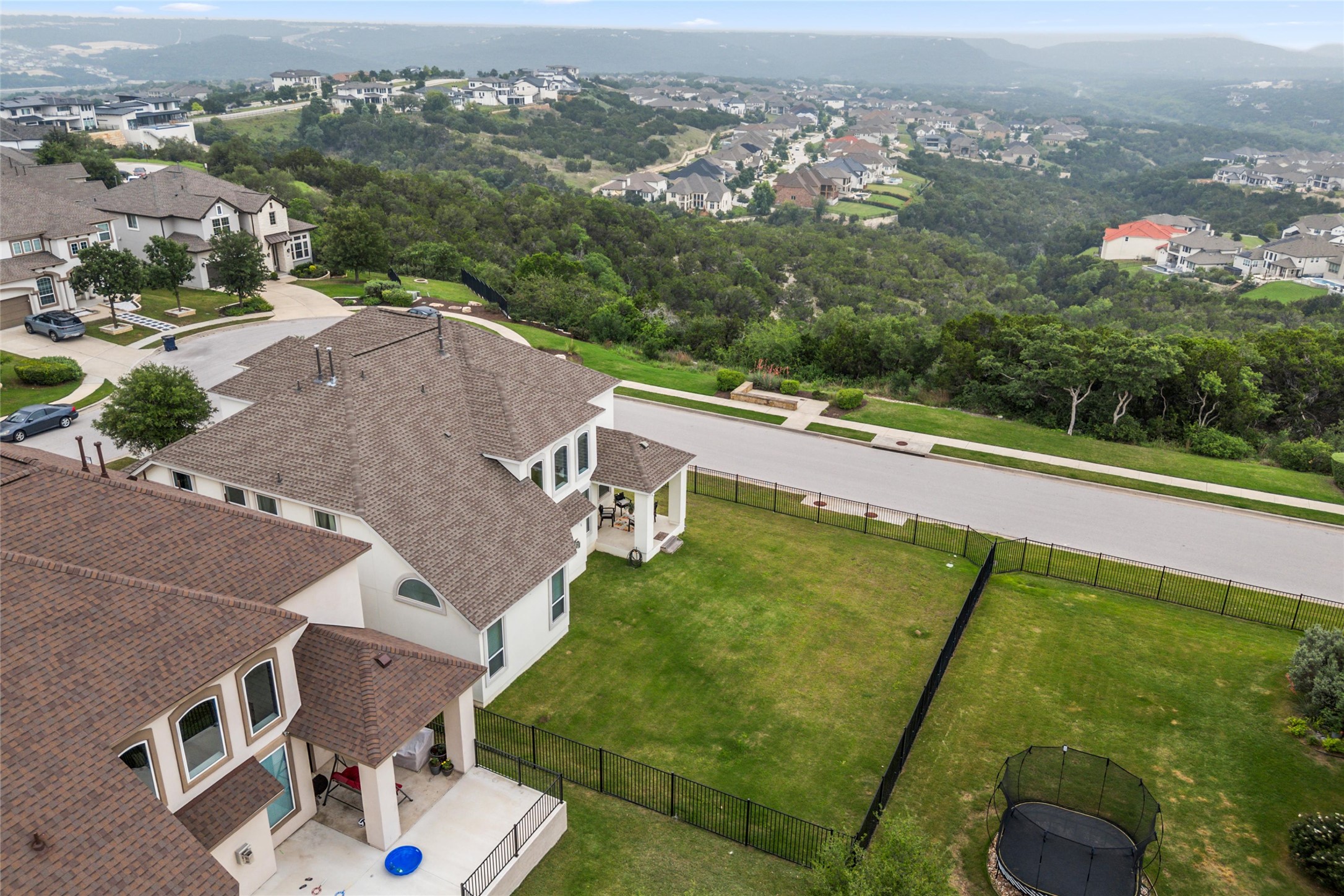 1733 Siena Sunset Road Leander, TX 78641 - Photo 6 of 40 Aerial perspective showcasing a residential property with a shingled roof, a large green lawn, and a black metal fence