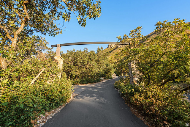 1141 South Oak Leaf Lane Springville, UT 84663 - Photo 16 of 147 Paved pathway featuring a stone column and lush surrounding greenery, framed by mature trees and a clear sky backdrop