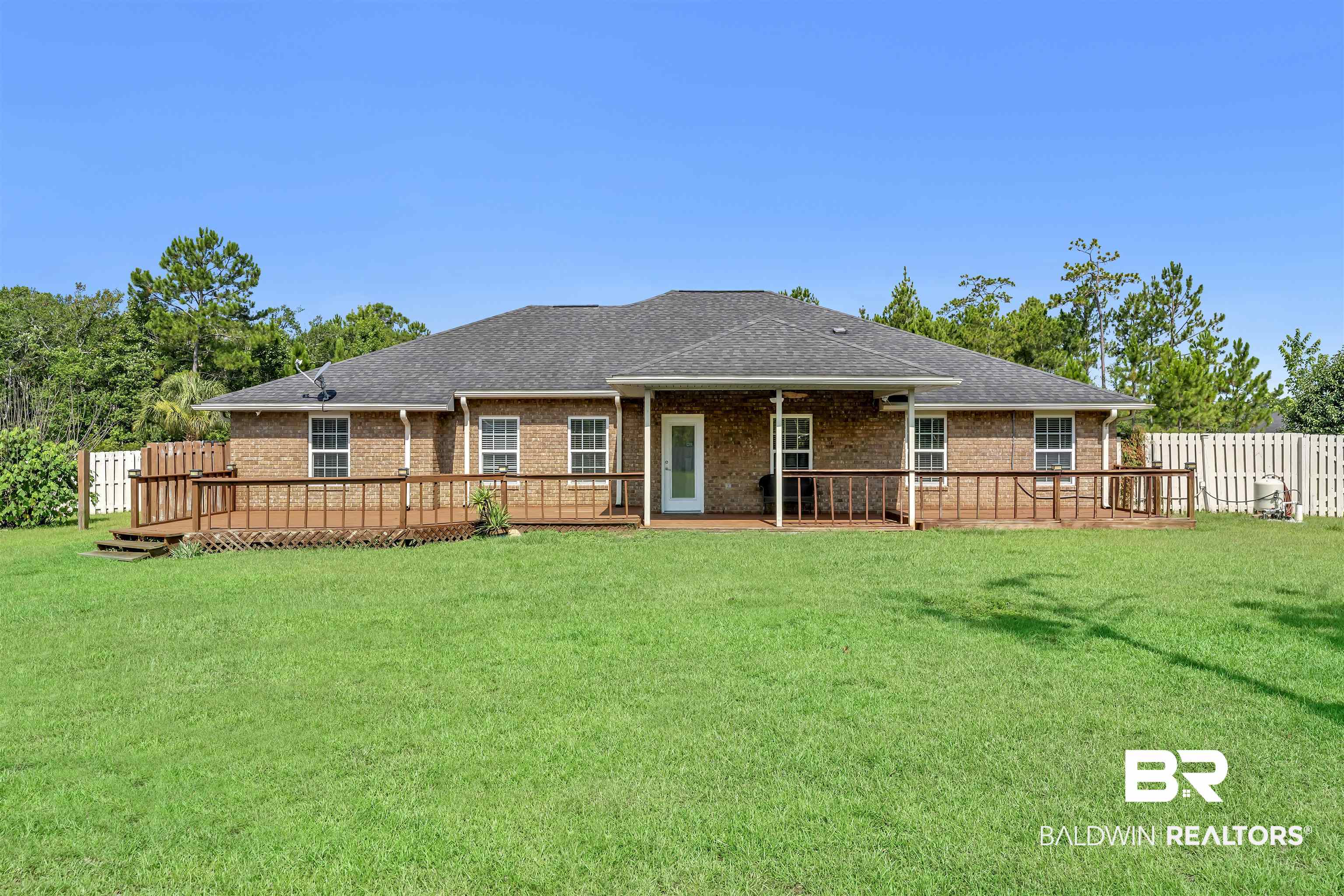 10147 Lyttleton Loop Lillian, AL 36549 - Photo 4 of 29 Expansive green lawn with a brick exterior home featuring a dark shingle roof, a generously sized wood deck, and a white picket fence partially enclosing the property