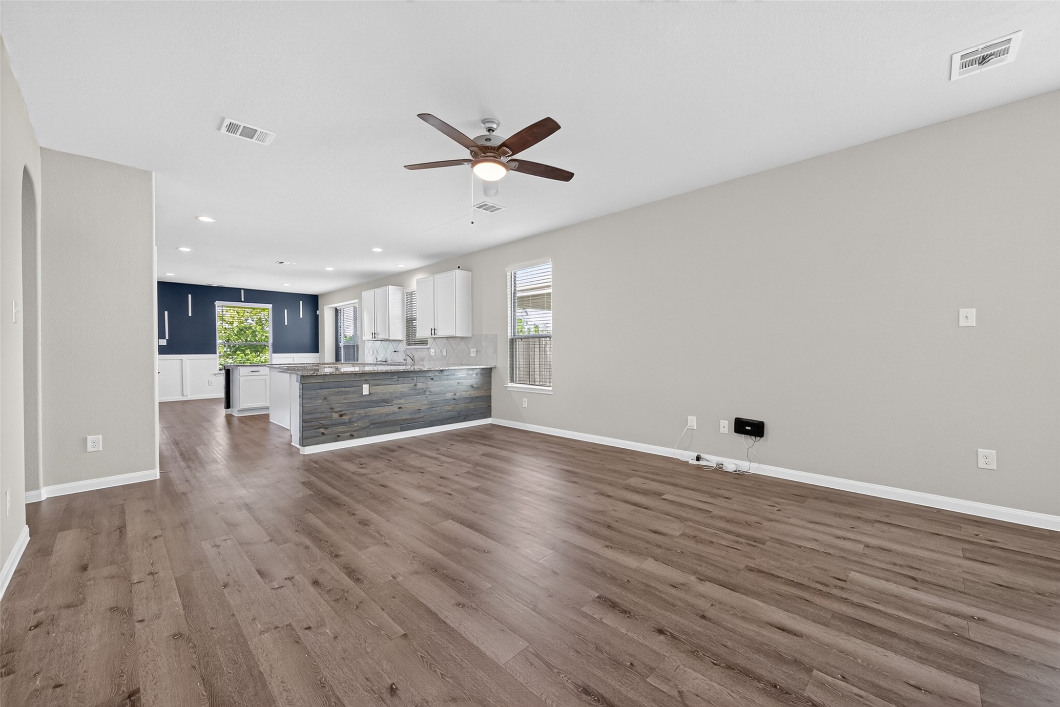 2526 Sturgeon Way Conroe, TX 77384 - Photo 7 of 49 This open-concept living space features modern wood flooring, a ceiling fan, and plenty of natural light. The kitchen boasts sleek white cabinetry, a stylish island with a textured finish, and a view of the backyard through large windows.