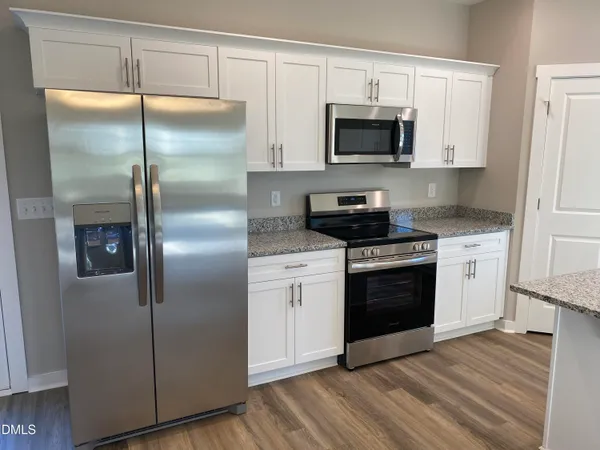 a kitchen with stainless steel appliances granite countertop a sink a microwave a refrigerator and white cabinets