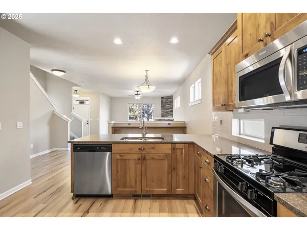 a kitchen with stainless steel appliances kitchen island granite countertop a stove top oven a sink dishwasher and cabinets with wooden floor