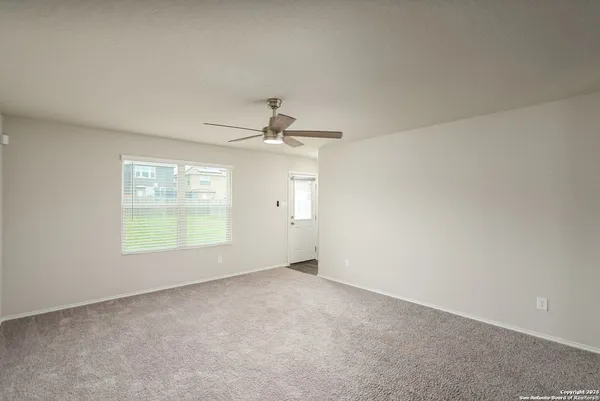 an empty room with a ceiling fan and kitchen view