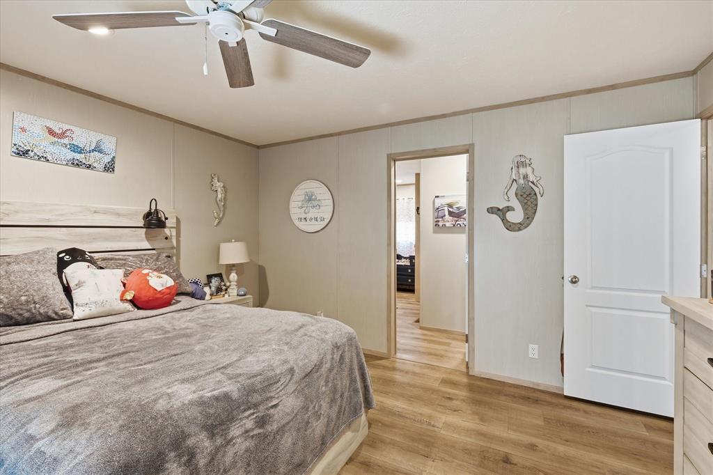 193 Firefly Drive Springtown, TX 76082 - Photo 15 of 32 Spacious bedroom featuring wood-finish flooring, light grey paneled walls, a ceiling fan with integrated lighting, a white two-panel door, and a light wood-finish headboard