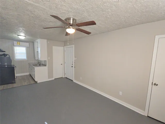 an empty room with a kitchen and a ceiling fan