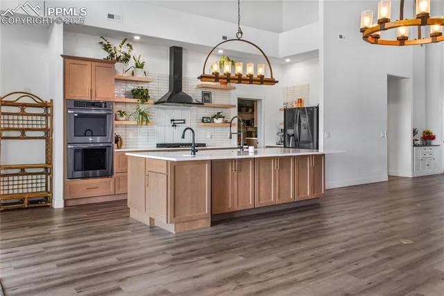 a kitchen with stainless steel appliances granite countertop a sink dishwasher a stove a refrigerator and a dining table with wooden floor