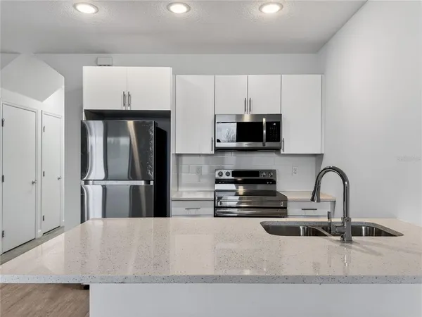 a kitchen with stainless steel appliances granite countertop a refrigerator a stove a sink and white cabinets