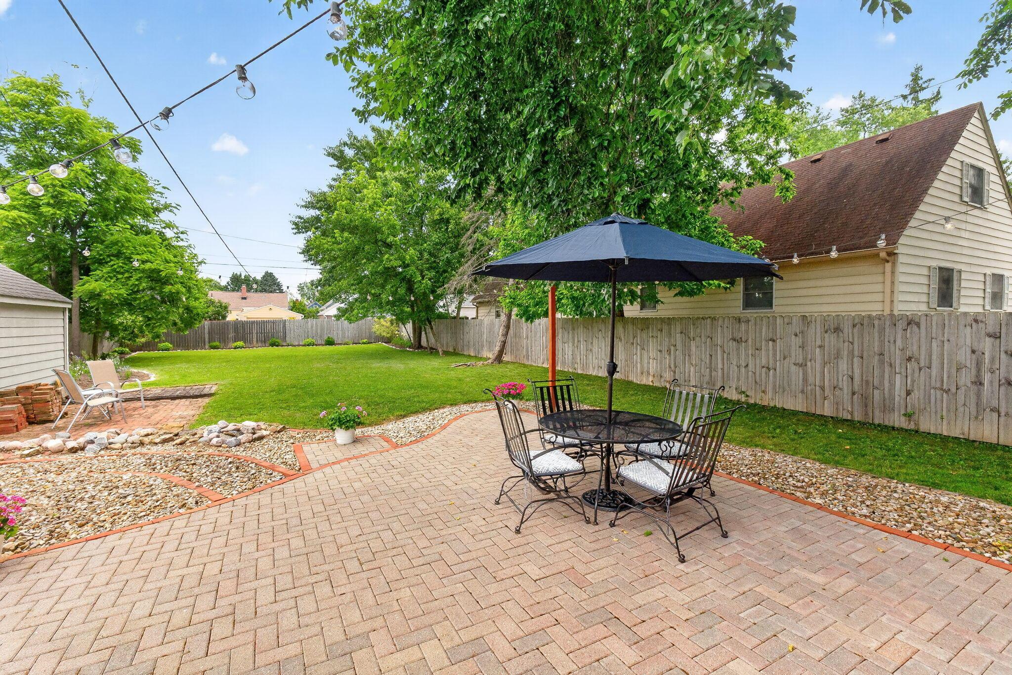 492 Wetmore Road Columbus, OH 43214 - Photo 3 of 55 Spacious backyard featuring a herringbone-patterned brick patio, a lush lawn, and a wood-panel fence