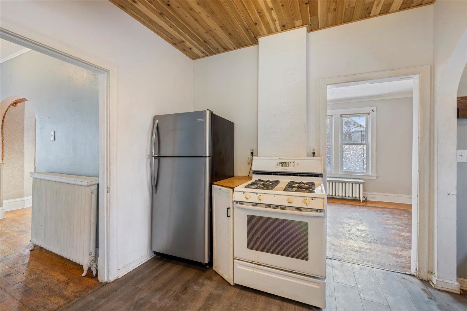 217 3rd Avenue Northwest Chisholm, MN 55719 - Photo 12 of 47 Kitchen featuring arched walkways, white gas range oven, freestanding refrigerator, radiator heating unit, and wooden ceiling