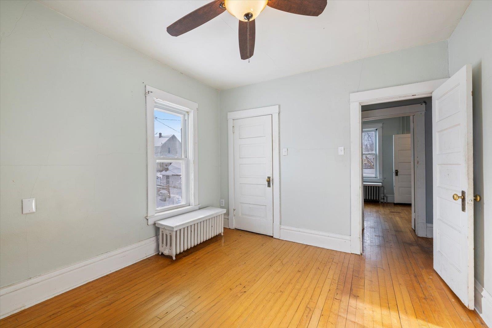 217 3rd Avenue Northwest Chisholm, MN 55719 - Photo 18 of 47 Unfurnished bedroom with radiator heating unit, light wood-type flooring, multiple windows, and a ceiling fan