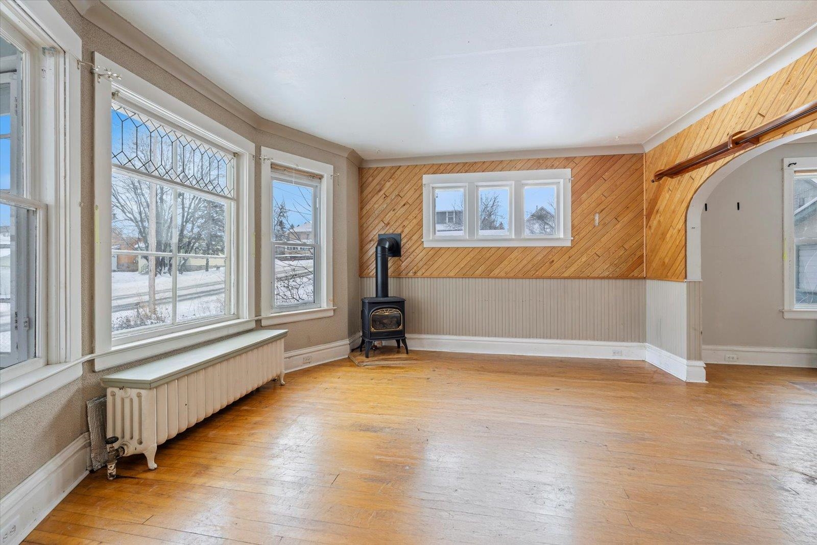 217 3rd Avenue Northwest Chisholm, MN 55719 - Photo 29 of 47 Empty room featuring wooden walls, radiator heating unit, light wood-style flooring, a wood stove, and arched walkways