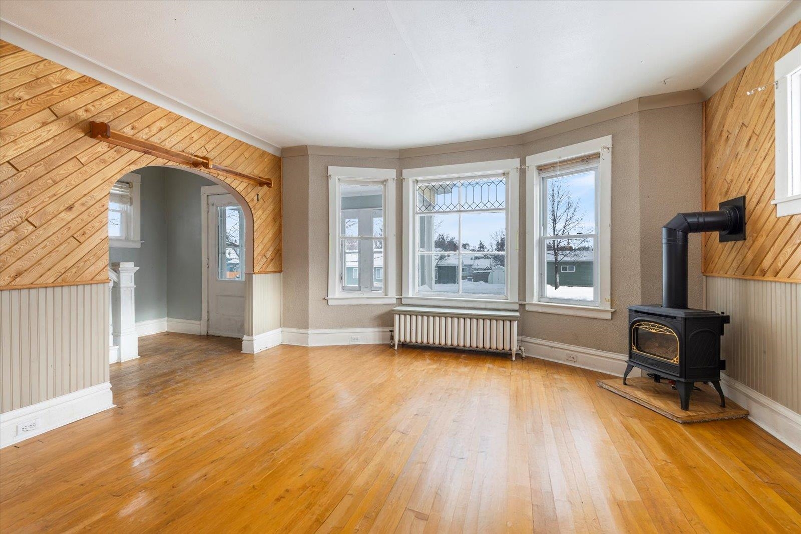 217 3rd Avenue Northwest Chisholm, MN 55719 - Photo 32 of 47 Unfurnished living room with wooden walls, arched walkways, a wood stove, radiator, and light wood finished floors