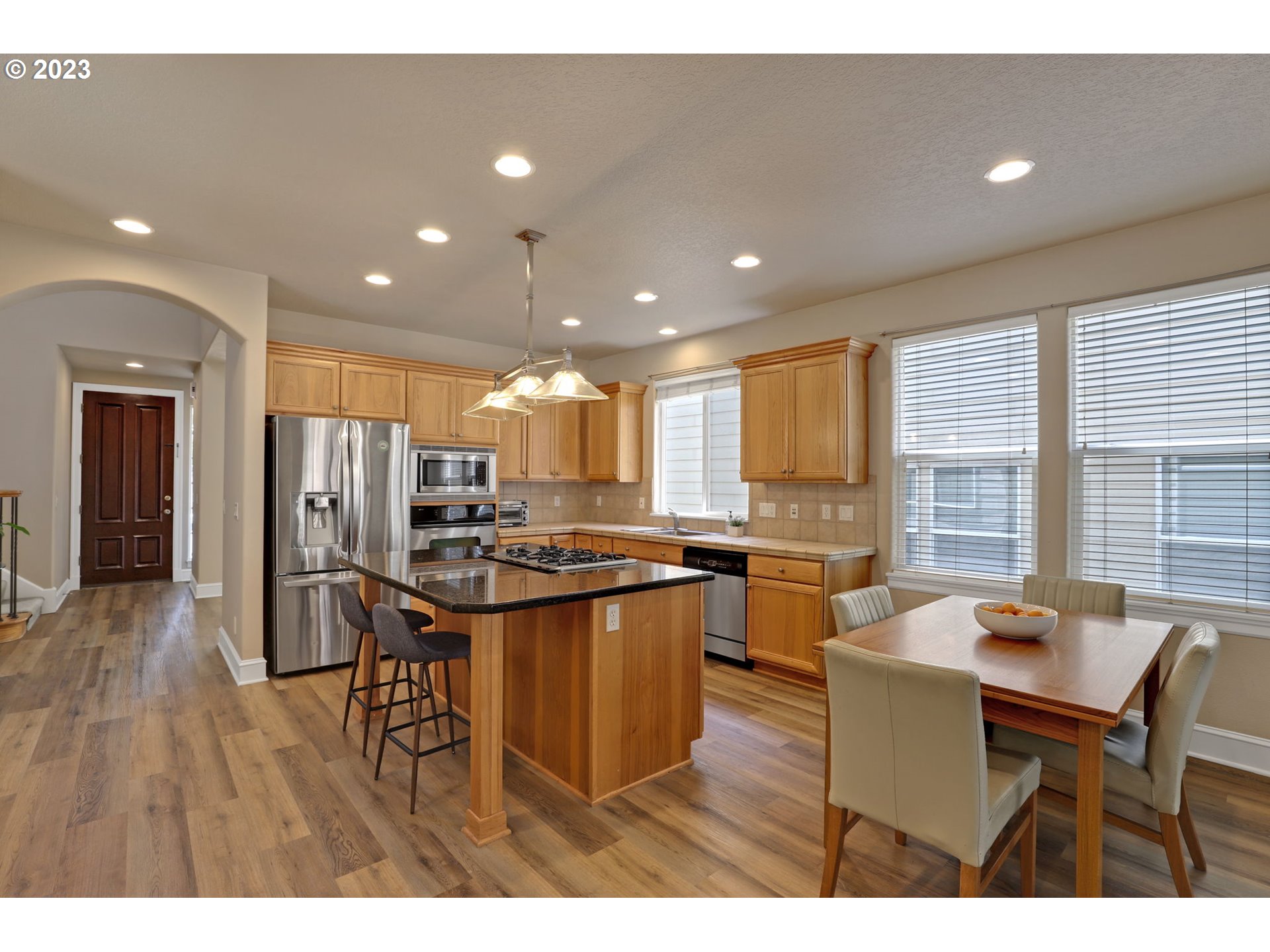 12799 Northwest Forest Spring Lane Portland, OR 97229 - Photo 7 of 30 a kitchen with stainless steel appliances granite countertop a stove top oven a refrigerator a sink and a dining table with wooden floor