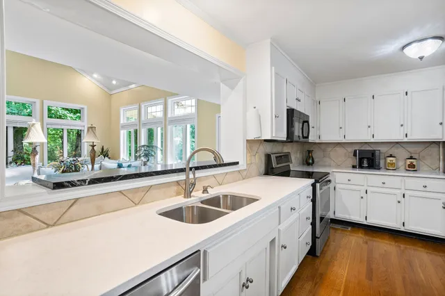 a kitchen with a sink dishwasher a stove top oven a refrigerator with white cabinets and wooden floor