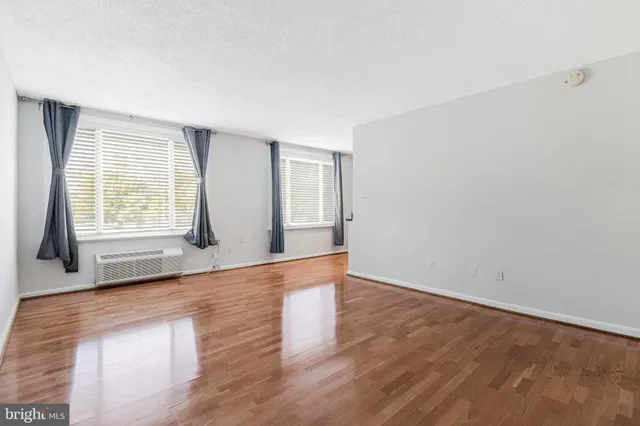 a view of an empty room with wooden floor and fan
