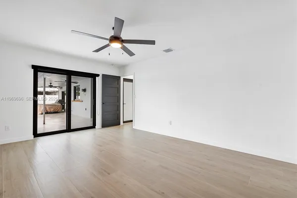 a view of an empty room with wooden floor and a ceiling fan