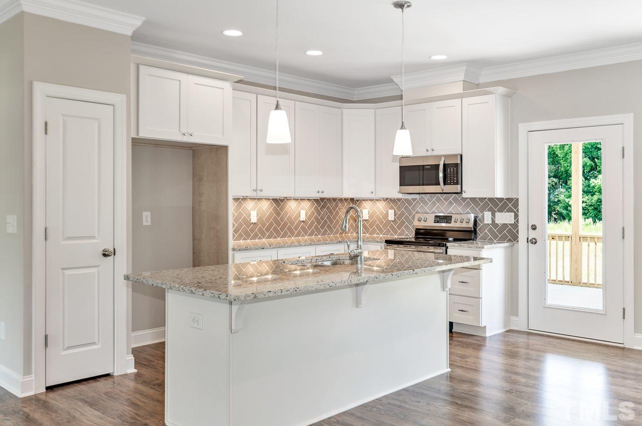 6733 Dwight Rowland Road Willow Spring, NC 27592 - Photo 6 of 25 Kitchen with herringbone back space and granite countertops central island with granite countertop over hang for dining or snacking