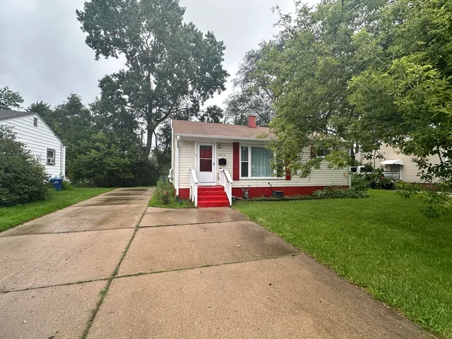 a view of a white house with a small yard and large trees