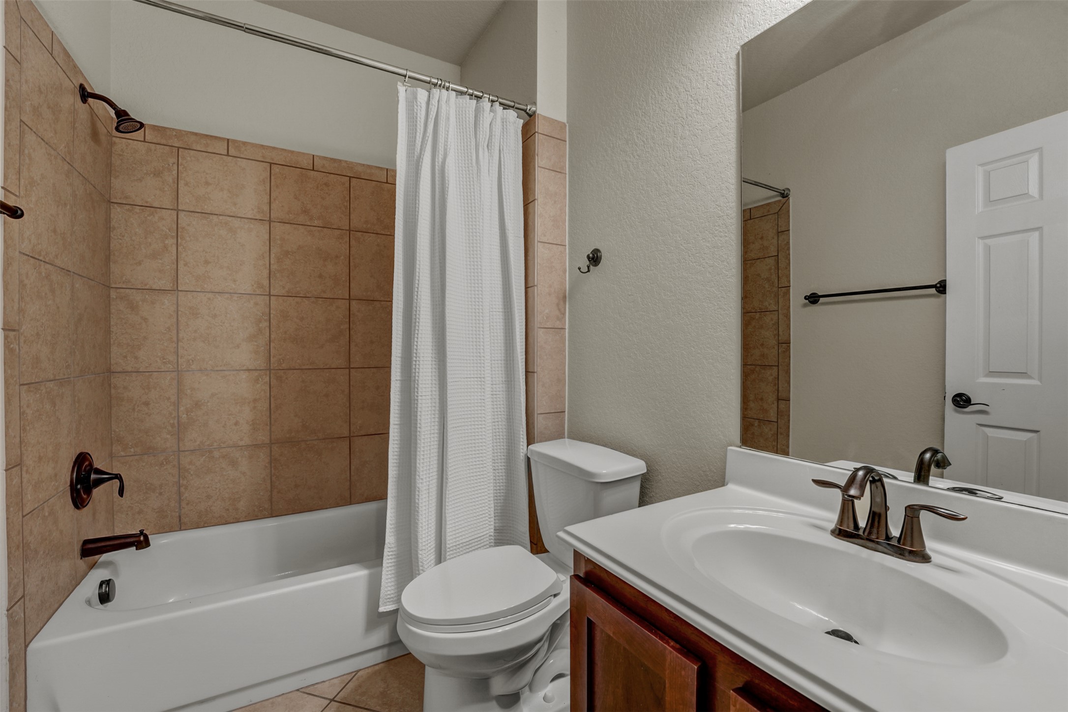 10506 Corvey Lane Helotes, TX 78023 - Photo 18 of 28 Bathroom featuring a textured wall, vanity, shower / tub combo with curtain, and light tile patterned floors