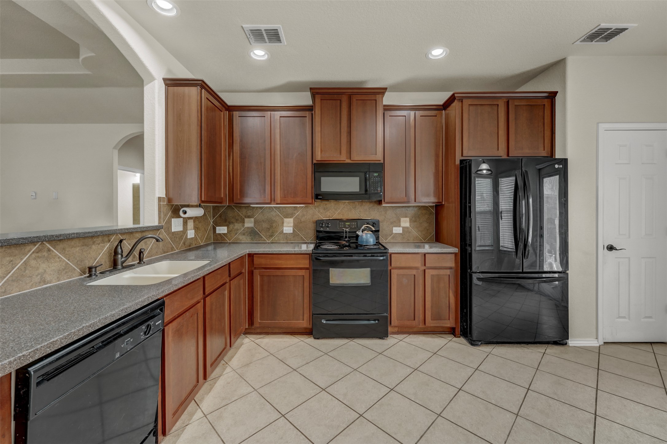10506 Corvey Lane Helotes, TX 78023 - Photo 10 of 28 Kitchen with black appliances, wood finish cabinets, decorative backsplash, recessed lighting, and dark stone counters