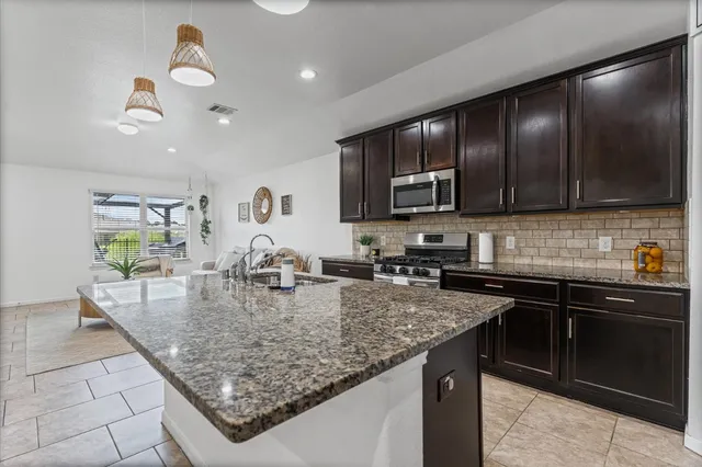 a kitchen with kitchen island granite countertop stainless steel appliances a sink a stove cabinets counter space and a window