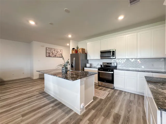 a kitchen with stainless steel appliances granite countertop a stove top oven a sink and white cabinets