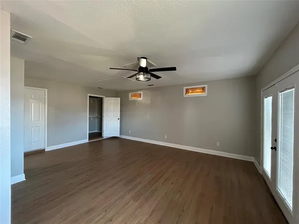 an empty room with wooden floor chandelier fan and windows