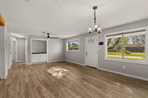a view of an empty room with window chandelier and wooden floor