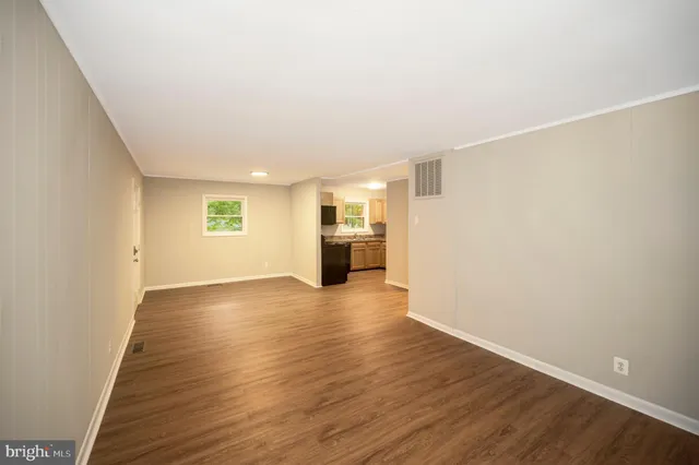 a view of empty room with wooden floor and kitchen