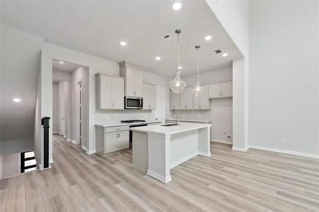 a kitchen with stainless steel appliances a stove top oven a refrigerator a sink and white cabinets with wooden floor