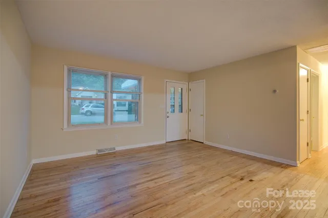 a view of an empty room with window and wooden floor