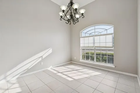 an empty room with chandelier fan and kitchen view