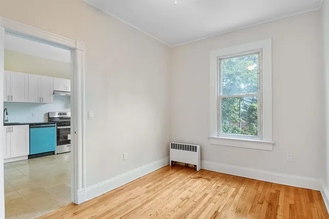 a view of an empty room with a window and wooden floor