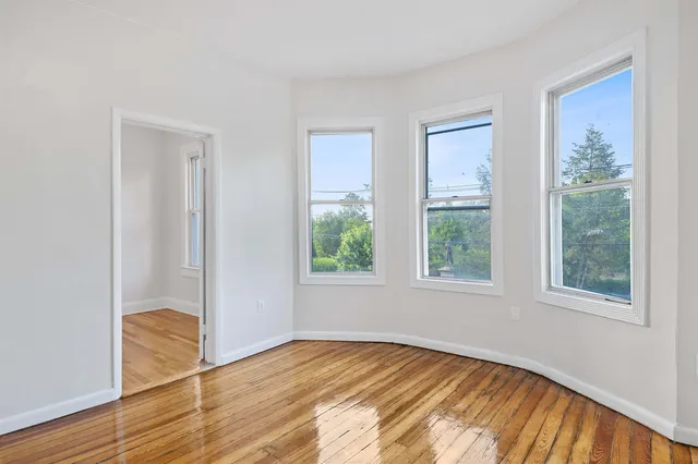 a view of an empty room with wooden floor and windows