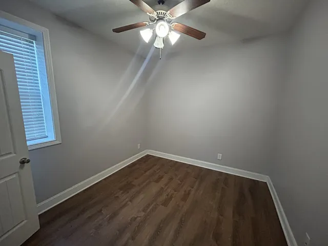 a view of an empty room with wooden floor and a fan