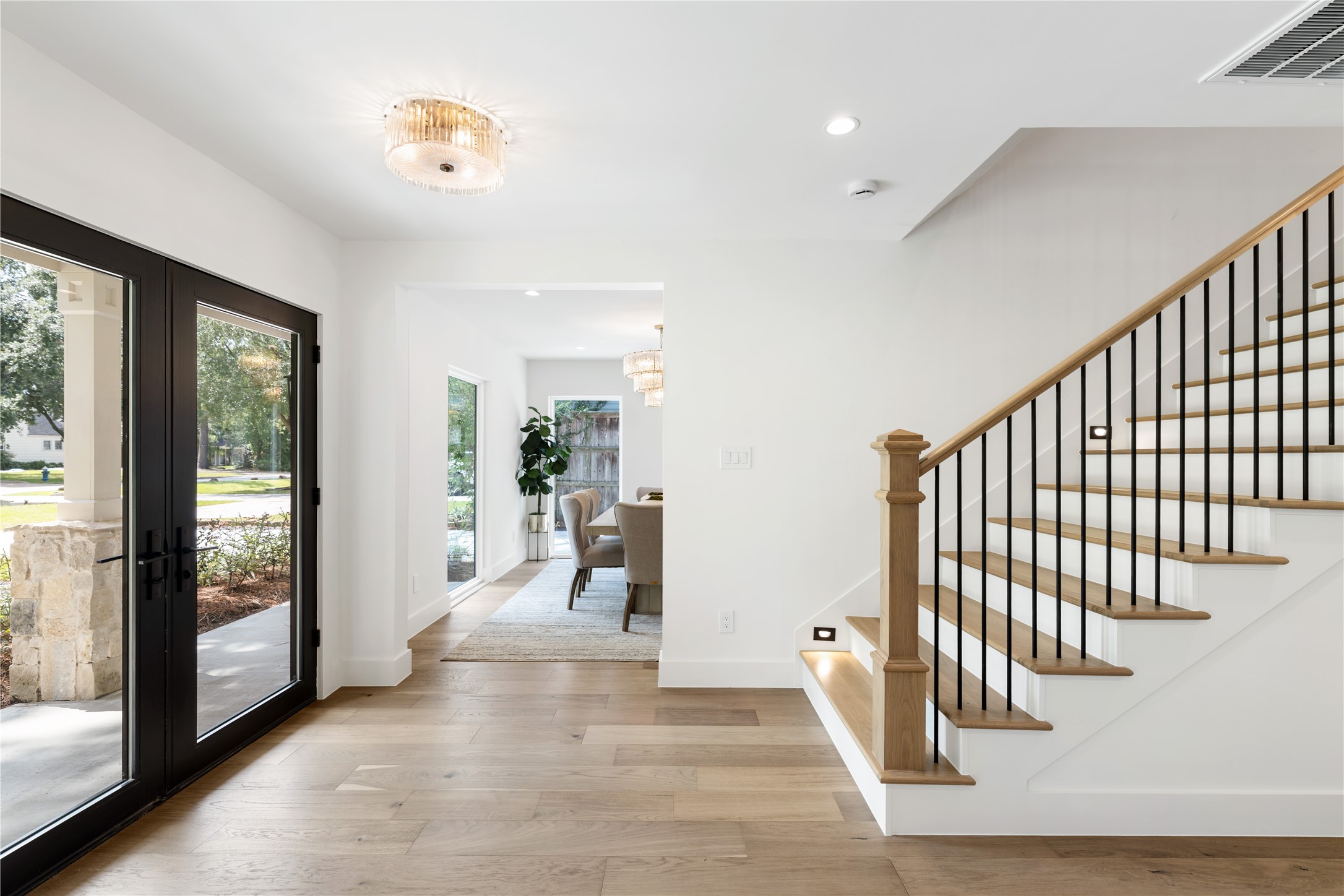 Bright entryway with double front doors, wide-plank wood floors, and open staircase.