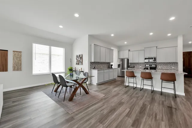 a living room with stainless steel appliances furniture wooden floor and a kitchen view