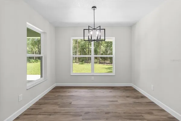 an empty room with wooden floor a chandelier and windows