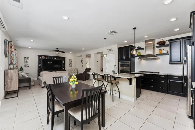 a kitchen with stainless steel appliances kitchen island granite countertop a dining table chairs and a refrigerator