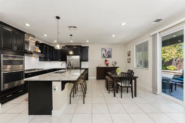 a open kitchen with stainless steel appliances kitchen island granite countertop a table chairs and a refrigerator
