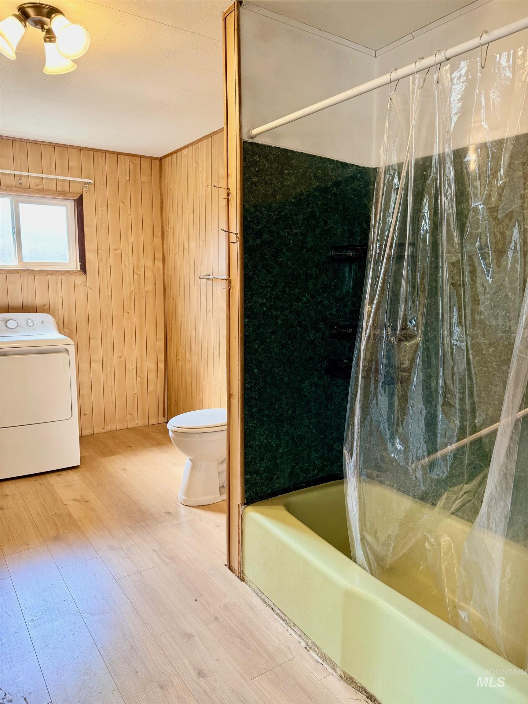 126 Aitken Road Weippe, ID 83553 - Photo 15 of 39 Bathroom featuring wood-finish flooring, natural wood paneling, a full bathtub with green wall surround, and a toilet