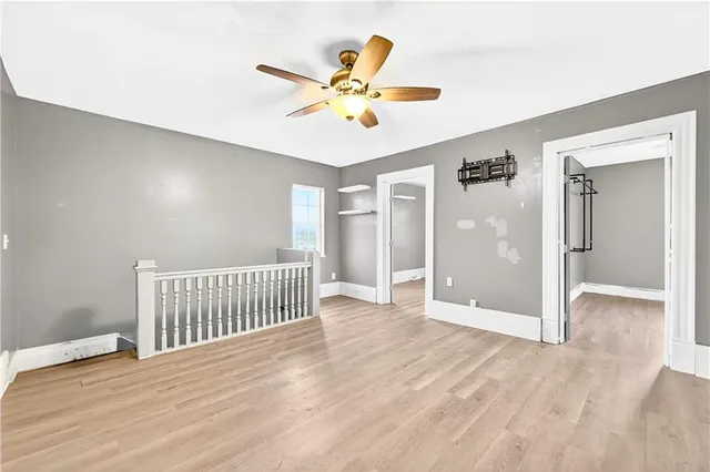 a view of an empty room with wooden floor and a ceiling fan